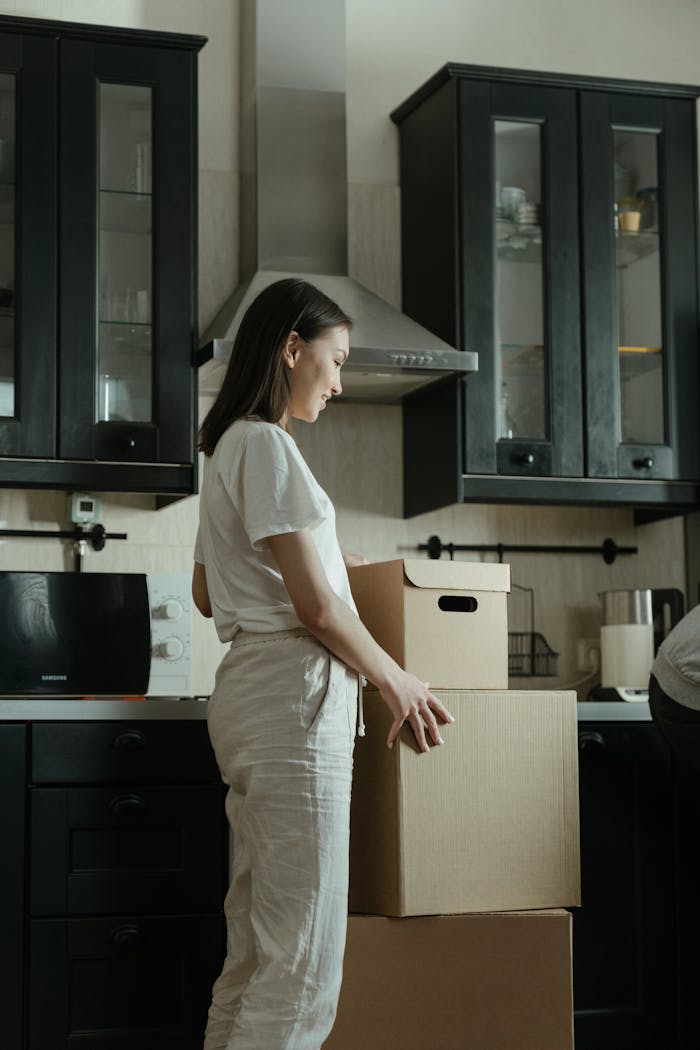 About A woman standing in a kitchen unpacking cardboard boxes in a modern apartment.